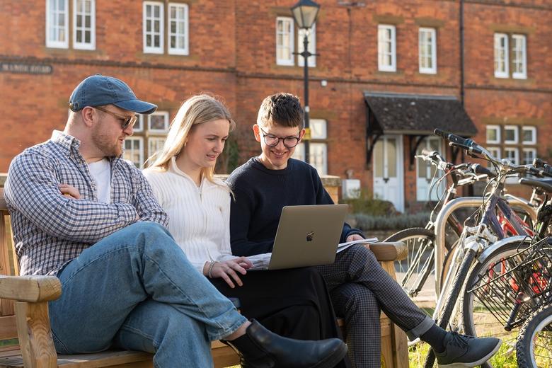 Three undergraduates sitting on a bench looking at a laptop computer