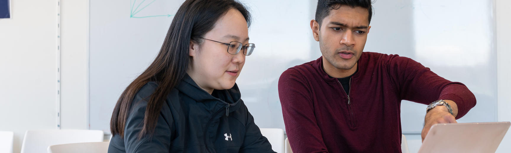 Two students discuss what is on a computer screen