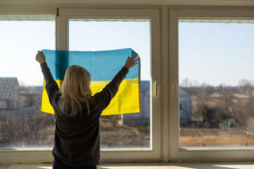 refugee woman holds flag of Ukraine up to window
